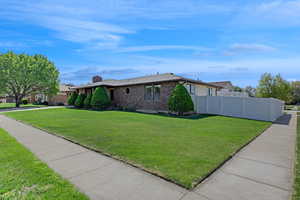 View of side of property with fence, a chimney, a lawn, and brick siding