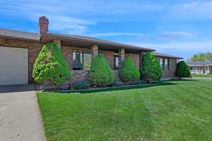 Ranch-style house with brick siding, an attached garage, a chimney, and a front yard
