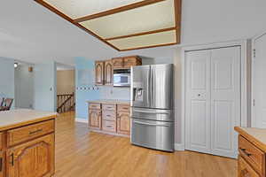 Kitchen with stainless steel refrigerator with ice dispenser, light countertops, light wood finished floors, and brown cabinetry