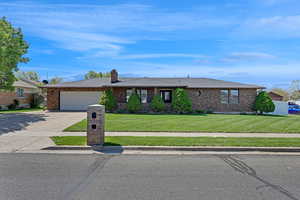 Ranch-style home featuring a garage, a front yard, driveway, and brick siding