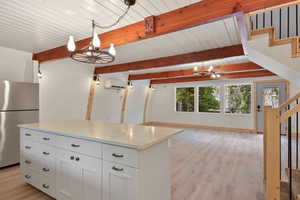 Kitchen featuring beamed ceiling, freestanding refrigerator, a notable chandelier, light wood-style floors, and white cabinetry