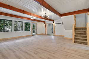 Unfurnished living room with a chandelier, a wall unit AC, a wealth of natural light, and light wood-style floors