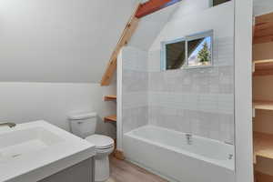 Bathroom featuring wood finished floors, lofted ceiling, toilet, a tub, and a sink
