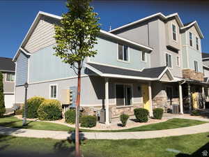 View of property with central AC unit, a front yard, with stone. stucco, and clapboard siding