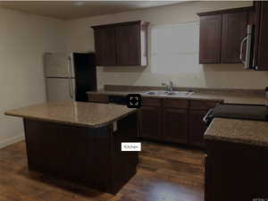 Kitchen with dark brown cabinetry, a kitchen island, dark wood-style floors, a sink, and stainless steel appliances