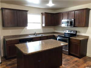 Kitchen with dark brown cabinetry, a center island, dark wood finished floors, a sink, and stainless steel appliances