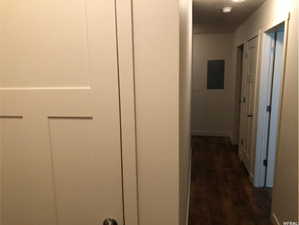 Hall with baseboards, dark wood-type flooring, and electric panel