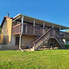 Back of property featuring a lawn, double stairs, and a large covered deck