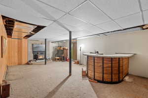 Finished below grade area featuring carpet flooring, a drop ceiling, and a wood stove
