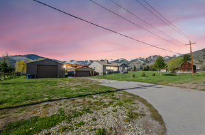View of front of home featuring dirt driveway, an outbuilding, fence, a mountain view, and a yard
