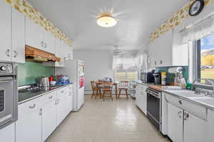 Kitchen with light countertops, white cabinetry, a baseboard heating unit, under cabinet range hood, and stainless steel appliances