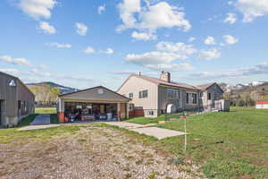 Back of house with a garage, a chimney, a lawn, a mountain view, and an outbuilding