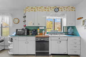 Kitchen with a sink, light countertops, black appliances, and white cabinetry