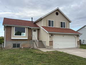 Split level home with a garage, concrete driveway, a front yard, brick siding, and roof with shingles