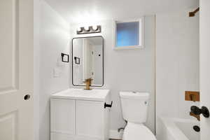 Bathroom with vanity, a textured ceiling, toilet, and shower / washtub combination