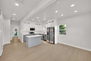 Kitchen with appliances with stainless steel finishes, baseboards, a kitchen island, and light wood finished floors