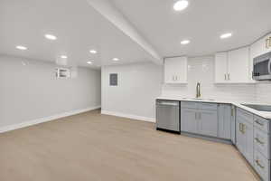 Kitchen featuring backsplash, appliances with stainless steel finishes, a sink, baseboards, and gray cabinetry