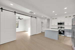 Kitchen with light wood-style floors, appliances with stainless steel finishes, a barn door, and visible vents