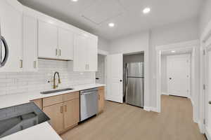 Kitchen with light wood-style floors, light countertops, a sink, appliances with stainless steel finishes, and backsplash