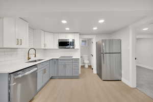 Kitchen with light countertops, a sink, light wood-style flooring, appliances with stainless steel finishes, and gray cabinetry