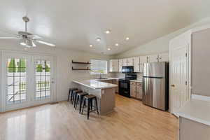 Kitchen featuring a breakfast bar, a sink, a peninsula, light wood-type flooring, and black appliances