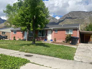 Single story home featuring a front yard, an attached carport, brick siding, a mountain view, and driveway