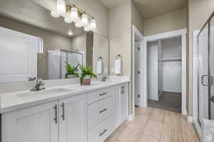 Bathroom featuring double vanity, a spacious closet, a shower stall, and a sink