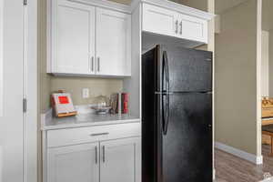 Kitchen with light countertops, white cabinets, freestanding refrigerator, and wood finished floors