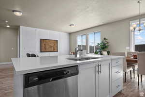 Kitchen with a textured ceiling, wood finished floors, dishwasher, a sink, and a notable chandelier