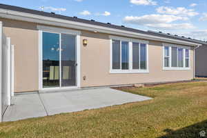 Rear view of property with a lawn, a patio area, and stucco siding