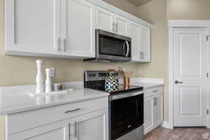 Kitchen with light wood-type flooring, light countertops, white cabinetry, and stainless steel appliances
