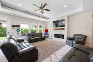 Carpeted living room with a ceiling fan, visible vents, a fireplace, a tray ceiling, and recessed lighting