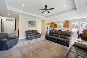 Living area featuring recessed lighting, a raised ceiling, ceiling fan with notable chandelier, and baseboards