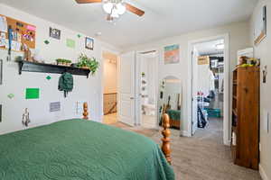 Bedroom with connected bathroom, light carpet, a walk in closet, a ceiling fan, and a closet