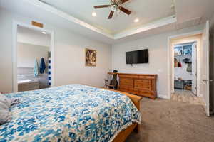 Carpeted bedroom with a raised ceiling, ceiling fan, recessed lighting, and visible vents