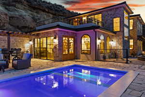 Rear view of house with a patio area, an outdoor pool, a balcony, and stone siding