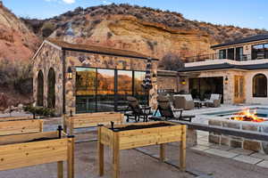 Rear view of house with an outdoor fire pit, stone siding, a mountain view, a balcony, and a patio