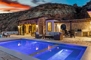 Pool at dusk with an outdoor structure, a mountain view, a storage structure, and a patio area