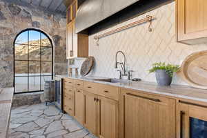 Kitchen with stone floors, glass insert cabinets, beverage cooler, light stone countertops, and a sink