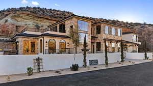 View of front of home with french doors, a fenced front yard, a mountain view, a balcony, and stone siding