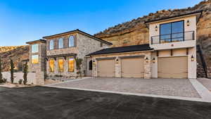 View of front of property with stone siding, stucco siding, a mountain view, decorative driveway, and a balcony