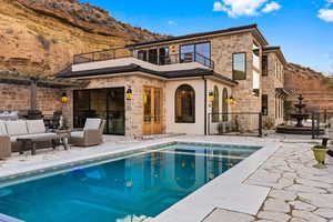 Back of house with a patio, an outdoor pool, a balcony, and stone siding