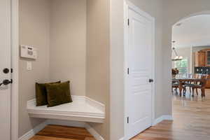 Mudroom featuring light wood-type flooring, arched walkways, baseboards, and an inviting chandelier