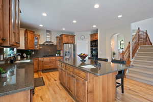 Kitchen featuring a sink, arched walkways, wall chimney range hood, and black appliances