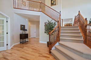 Stairs featuring baseboards, wood finished floors, and a towering ceiling
