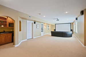 Home theater featuring light colored carpet, a sink, baseboards, and visible vents