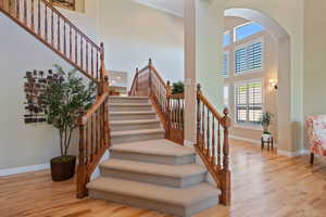 Staircase featuring baseboards, arched walkways, a towering ceiling, and wood finished floors