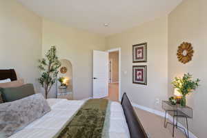 Bedroom featuring baseboards, arched walkways, and light colored carpet