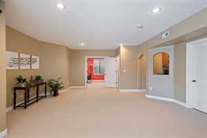 Interior space featuring light carpet, arched walkways, recessed lighting, baseboards, and visible vents