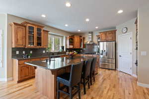 Kitchen with brown cabinets, appliances with stainless steel finishes, a sink, a kitchen island with sink, and wall chimney exhaust hood